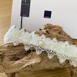 May include: White lace garter with a satin ribbon and a pearl embellishment.
