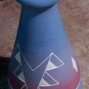 May include: A blue and pink ceramic vase with a geometric design. The vase has a white rim and a white base.