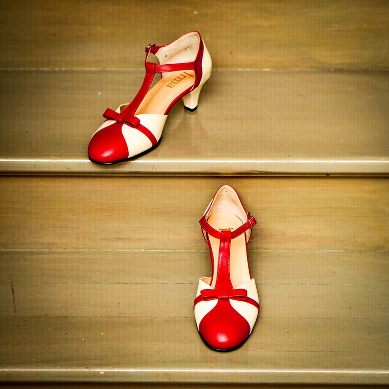 Pu&ograve; includere: Un paio di scarpe con tacco rosso e bianco con un design a T. Le scarpe sono su una scala di legno.