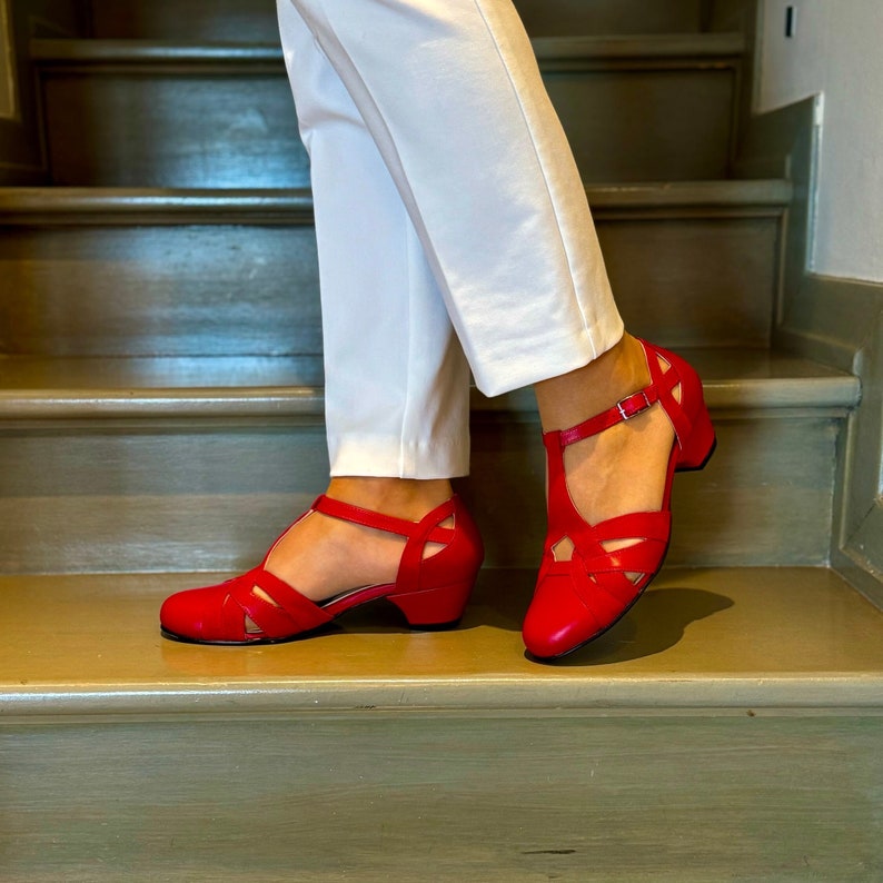 May include: Red leather heeled sandals with ankle straps and a criss-cross design on the front. The sandals have a low block heel.