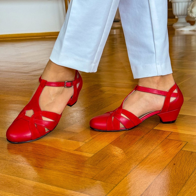 May include: A pair of red leather heeled sandals with a t-strap and cut-out detailing. The sandals have a low block heel.