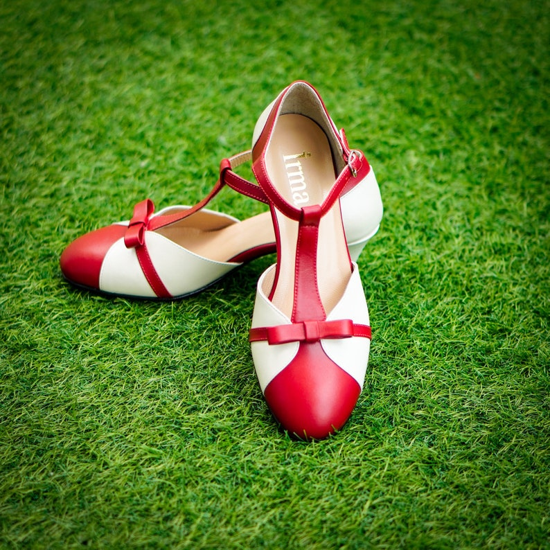 Pu&ograve; includere: Un paio di scarpe da donna rosse e bianche con un fiocco sulla punta e la parola "Irma" all'interno della scarpa.