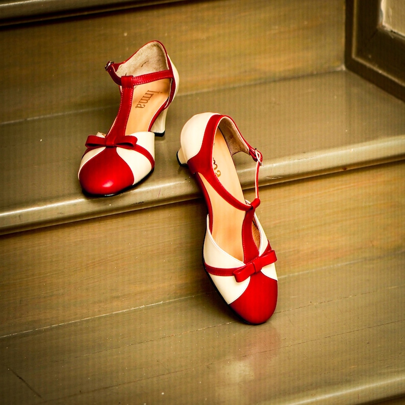 Pu&ograve; includere: Un paio di scarpe con tacco rosso e bianco con un design a T. Le scarpe sono su una scala di legno.