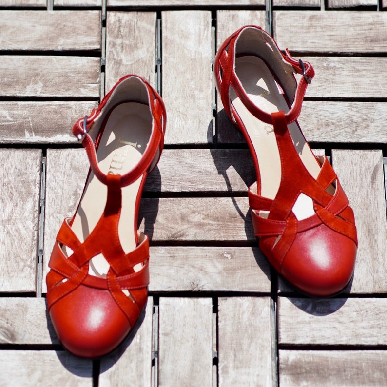 May include: A pair of red leather sandals with a t-strap design. The sandals have a delicate ankle strap and a closed toe.