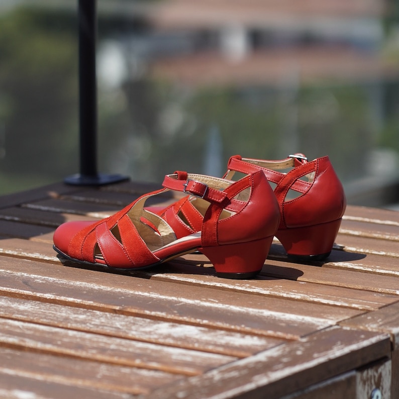 May include: A pair of red leather heeled sandals with a criss-cross strap design. The sandals have a chunky heel and an open toe.