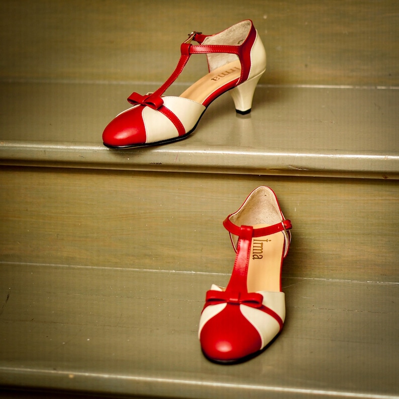 Pu&ograve; includere: Un paio di scarpe con tacco rosso e bianco con un design a T. Le scarpe hanno un dettaglio a fiocco sulla punta e il nome del marchio "Irma" &egrave; stampato sulla soletta.