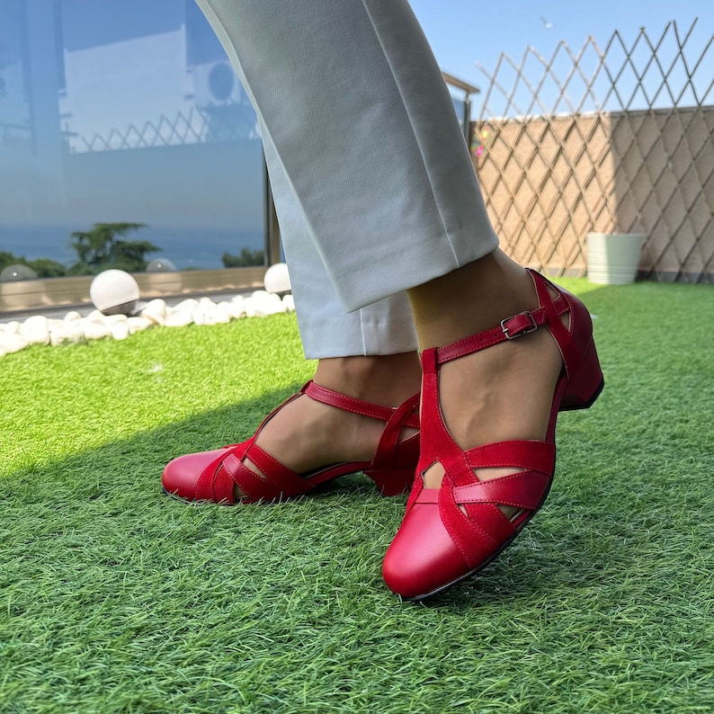 May include: Red leather heeled sandals with a criss-cross strap design and an ankle strap with a buckle closure.