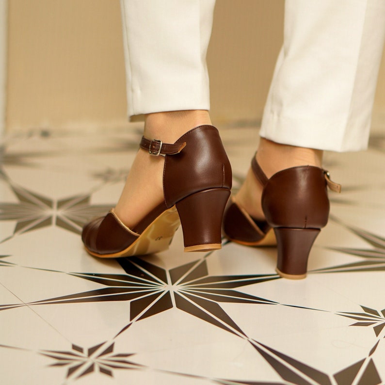 May include: A pair of brown leather heeled sandals with ankle straps. The sandals have a closed toe and a block heel.
