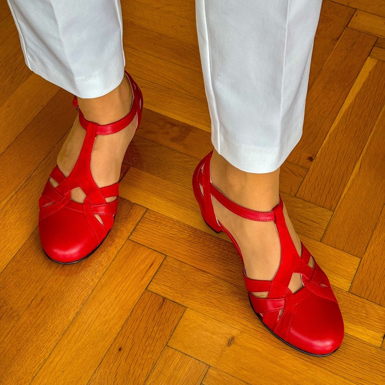 May include: Red leather sandals with a criss-cross strap design. The sandals have a closed toe and a low heel.