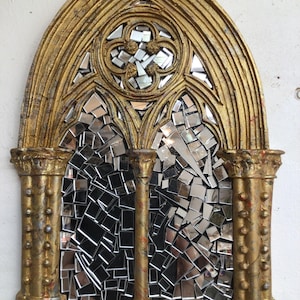 Puede incluir: Un espejo decorativo en forma de arco pintado en oro con un mosaico de pequeños trozos de espejo. El espejo está enmarcado con un diseño detallado y ornamentado.