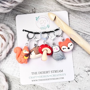 May include: Set of five colorful stitch markers featuring a squirrel, hedgehog, mushroom, owl, and fox. The markers are attached to silver rings and are displayed on a white card with the text "THE DESERT STREAM" and "CRAFT • DESIGN • CREATIVITY".