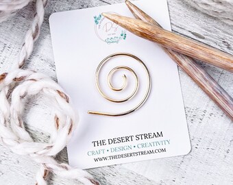 May include: Gold metal spiral stitch marker on a white card with the text "THE DESERT STREAM" and "CRAFT • DESIGN • CREATIVITY" and the website address "WWW.THEDESERTSTREAM.COM".