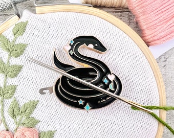 May include: Black snake with stars and hearts embroidery hoop art. The snake is coiled and has a needle threaded through it.