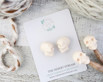 May include: Three white ceramic skull beads on a white card with the text "THE DESERT STREAM CRAFT • DESIGN • CREATIVITY WWW.THEDESERTSTREAM.COM".