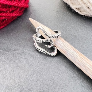 May include: Silver octopus-shaped stitch marker for knitting or crocheting. The marker is on a wooden knitting needle.