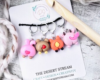 May include: Set of four colourful animal stitch markers with silver rings. The markers are shaped like the back ends of a bunny, bear, fox, and cow. The markers are on a white card with the text "THE DESERT STREAM" and "CRAFT • DESIGN • CREATIVITY" and a website address.