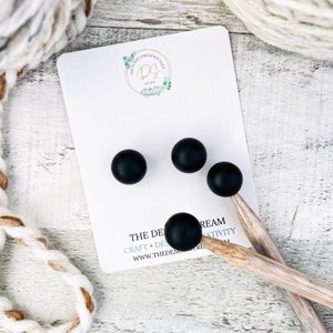 May include: Four black wooden knitting needles with black tips. The needles are on a white card with the text "The Desert Stream Boutique" and a logo.