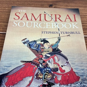 May include: The Samurai Sourcebook by Stephen Turnbull, a book cover featuring an illustration of a samurai on horseback riding through water.