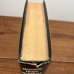 Może przedstawiać: Książka w twardej oprawie z czarnym grzbietem i tytułem "Rossell Hope Robbins" w białych literach. Strony są postarzałe w kolorze brązowym, a krawędzie lekko zużyte. Książka jest ustawiona na drewnianej powierzchni.