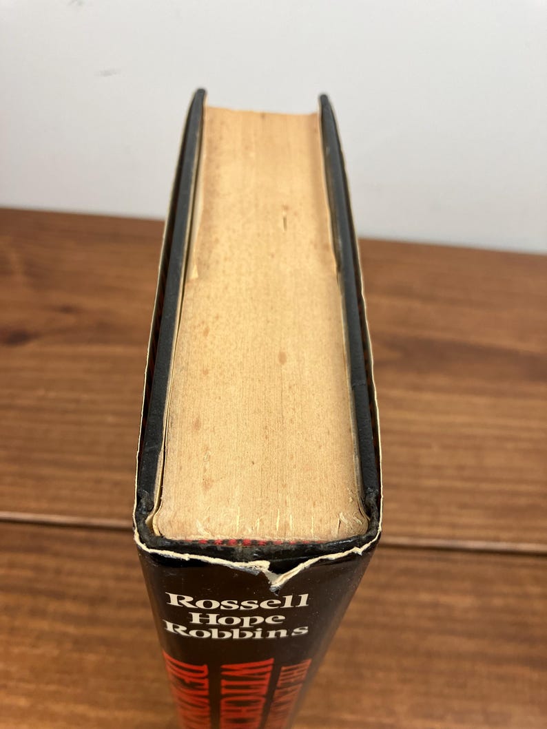 Może przedstawiać: Książka w twardej oprawie z czarnym grzbietem i tytułem "Rossell Hope Robbins" w białych literach. Strony są postarzałe w kolorze brązowym, a krawędzie lekko zużyte. Książka jest ustawiona na drewnianej powierzchni.