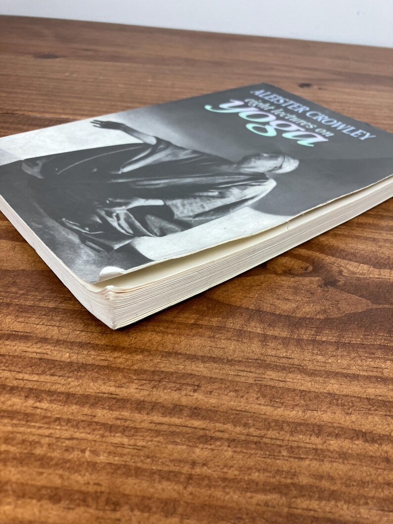 May include: A book titled "Aleister Crowley: Eight Lectures on Yoga" is shown on a wooden surface. The book cover features a black and white image of a robed figure. The title is in a stylized font with a teal accent.