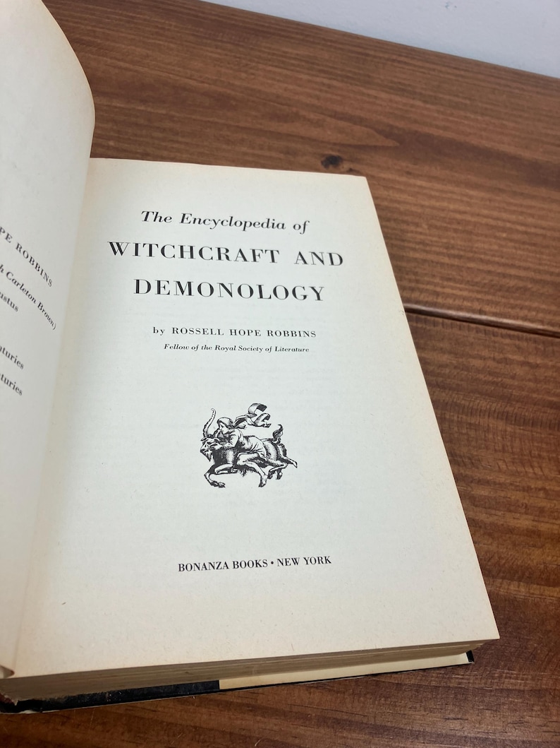 Może przedstawiać: Otwarta książka zatytułowana "The Encyclopedia of Witchcraft and Demonology" autorstwa Rossella Hope Robbinsa. Tytuł książki jest pogrubioną czcionką szeryfową. Logo Bonanza Books znajduje się na dole. Książka jest otwarta na drewnianej powierzchni.