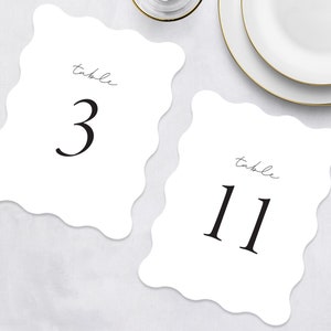 May include: Two white table number cards with scalloped edges. The card on the left says "table 3" and the card on the right says "table 11".