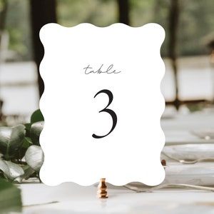May include: White table number card with scalloped edges. The card has the word "table" written in cursive and the number "3" in a large, bold font.