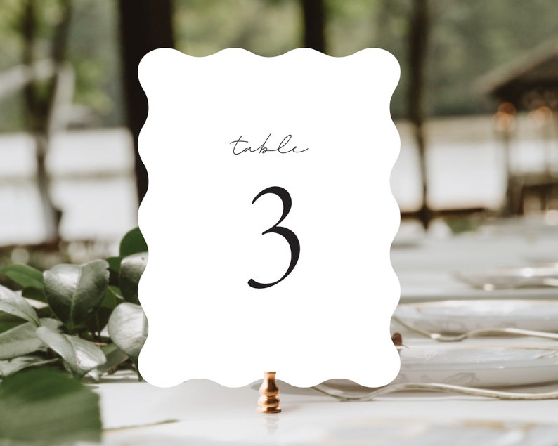 May include: White table number card with scalloped edges. The card has the word "table" written in cursive and the number "3" in a large, bold font.