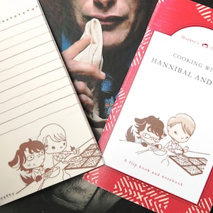 Könnte beinhalten: Ein rotes und weißes Flipbook und Notizbuch mit dem Titel "Cooking with Hannibal and Will" und dem Text "A flip book and notebook". Das Cover zeigt eine Cartoon-Illustration von zwei Männern beim Kochen.