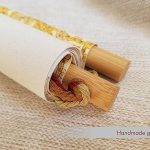 May include: Rolled canvas with wooden dowels, featuring a yellow floral patterned fabric and a bundle of colorful embroidery floss. The text "Handmade goodness" is visible. This item is perfect for craft enthusiasts.