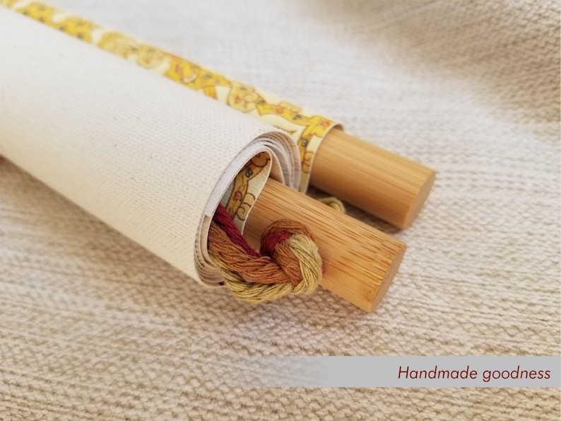 May include: Rolled canvas with wooden dowels, featuring a yellow floral patterned fabric and a bundle of colorful embroidery floss. The text "Handmade goodness" is visible. This item is perfect for craft enthusiasts.