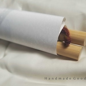 May include: A rolled up canvas print with wooden dowels and a brown string attached. The print is on a white surface.