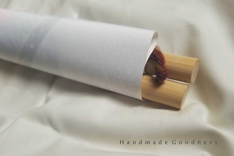 May include: A rolled up canvas print with wooden dowels and a brown string attached. The print is on a white surface.