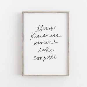 Könnte beinhalten: Gerahmter Druck mit dem handschriftlichen Text „throw kindness around like confetti“ in Schwarz auf weißem Hintergrund. Der Rahmen ist helles Holzfarben, der Druck ist mittig platziert.