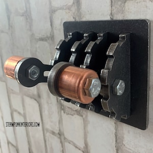 May include: A black metal light switch with a copper toggle handle and three gears. The switch is mounted on a brick wall.