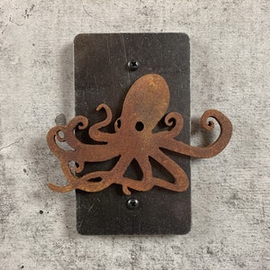 May include: A rusty metal octopus wall decor with a black metal background. The octopus is attached to the background with screws.
