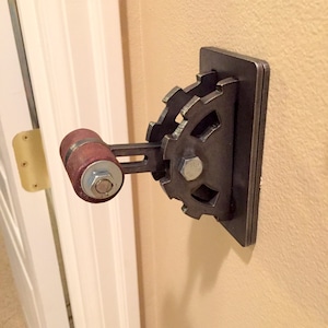 Op de afbeelding: Een metalen lichtschakelaar met een tandwielvormige hendel en een bruine houten knop. De schakelaar is gemonteerd op een muur.