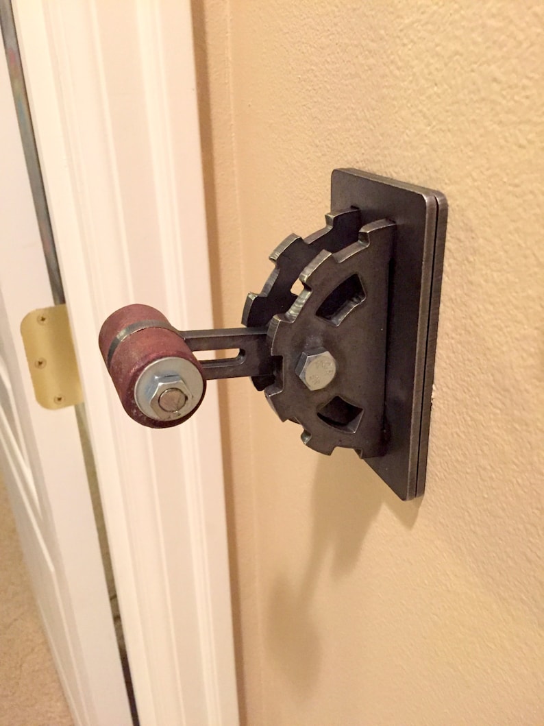 Op de afbeelding: Een metalen lichtschakelaar met een tandwielvormige hendel en een bruine houten knop. De schakelaar is gemonteerd op een muur.