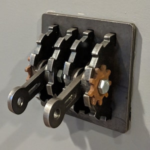 May include: A metal light switch with a steampunk design featuring multiple gears and levers. The switch is mounted on a metal plate.
