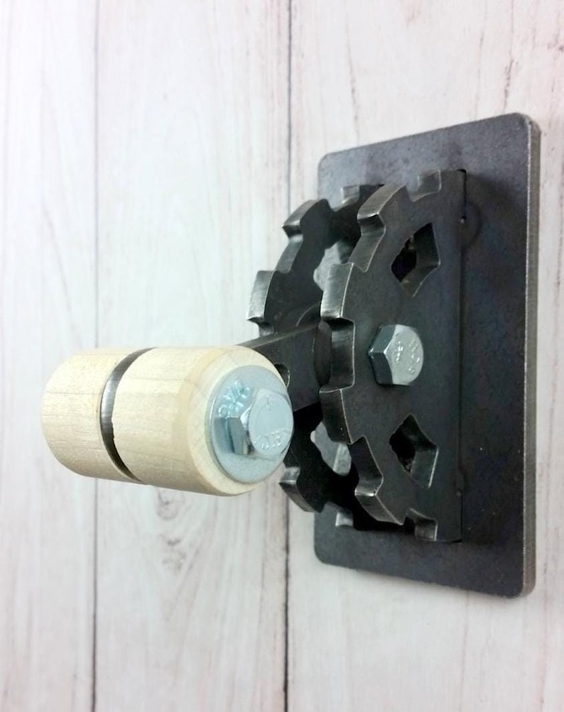 Op de afbeelding: Een metalen lichtschakelaar met een houten handvat en een tandwielvormig ontwerp. De schakelaar is gemonteerd op een witte muur.