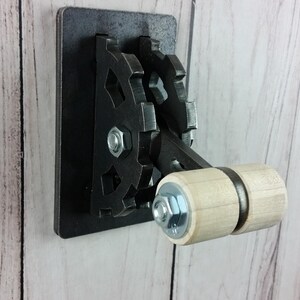 Op de afbeelding: Een zwarte metalen lichtschakelaar met een houten tandwielhendel. De schakelaar heeft een decoratief tandwielontwerp.