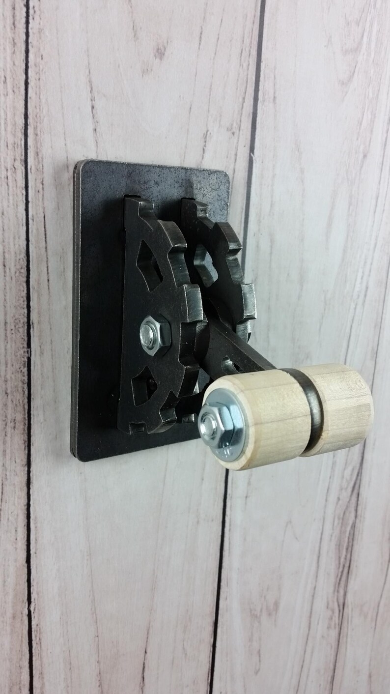 Op de afbeelding: Een zwarte metalen lichtschakelaar met een houten tandwielhendel. De schakelaar heeft een decoratief tandwielontwerp.