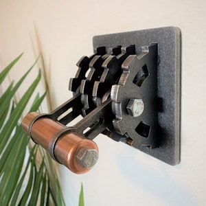 May include: A metal light switch with a copper toggle and a gear design. The switch is mounted on a gray metal plate.
