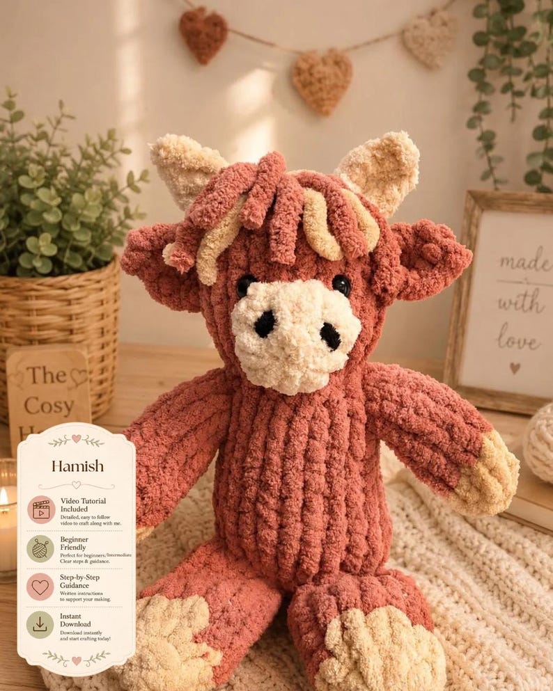 May include: A handmade, plush Highland cow named Hamish, in shades of pink and cream. The stuffed animal has a textured, soft appearance, with a white face and black eyes. The image includes a sign with the name "Hamish" and details about a video tutorial.
