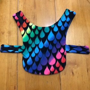 May include: A black fleece dog vest with a rainbow raindrop pattern. The vest has adjustable straps.