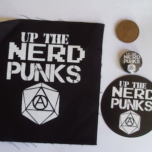 Può includere: Una toppa bianca e nera con il testo "Up the Nerd Punks" e un simbolo geometrico bianco. Ci sono due bottoni rotondi bianchi e neri con lo stesso testo e simbolo.