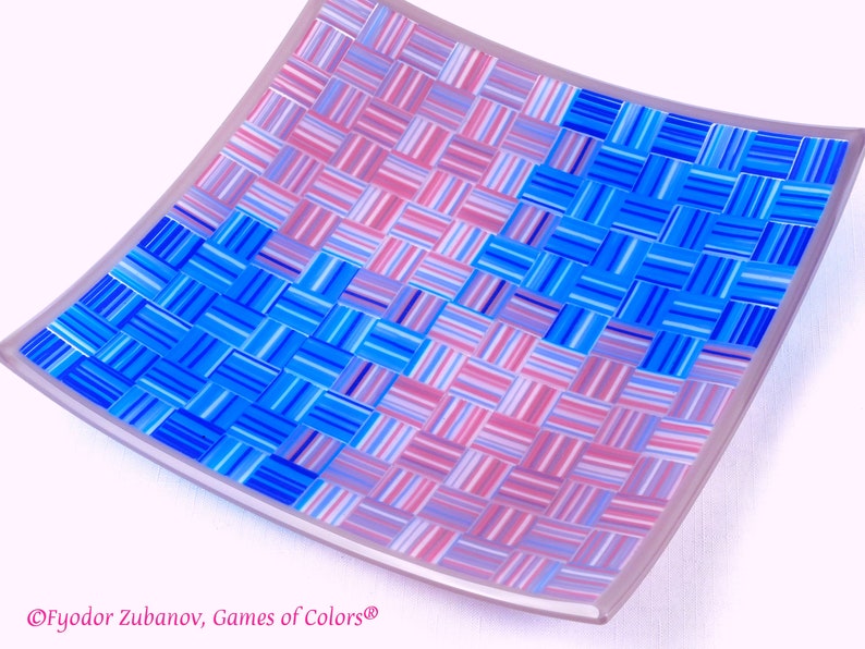 May include: A square glass dish with a woven pattern in shades of blue and pink. The dish is slightly curved and has a white border.