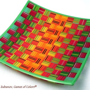 May include: A square, green-rimmed glass plate with a woven pattern of colorful stripes in red, orange, yellow, green, and blue.