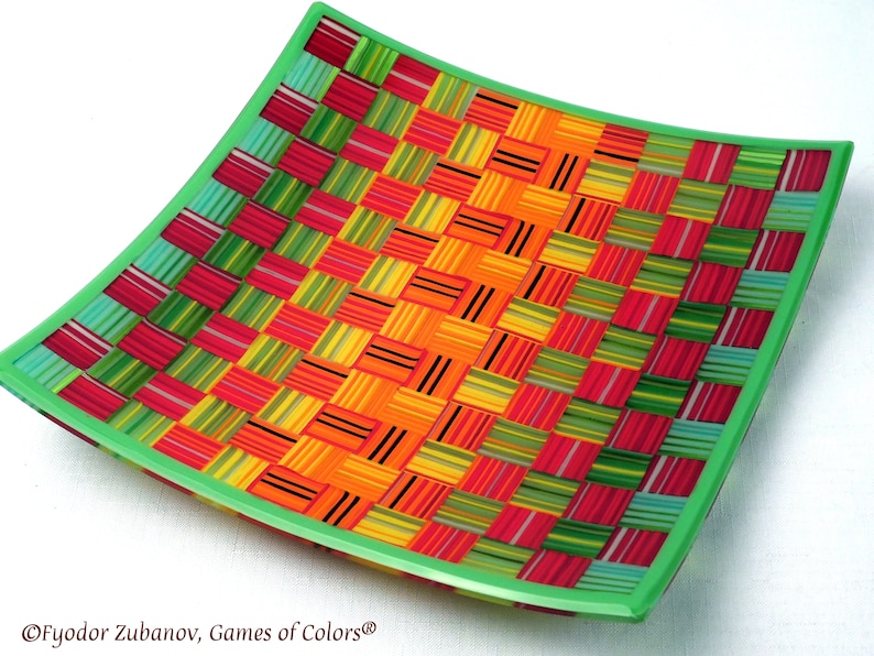 May include: A square, green-rimmed glass plate with a woven pattern of colorful stripes in red, orange, yellow, green, and blue.